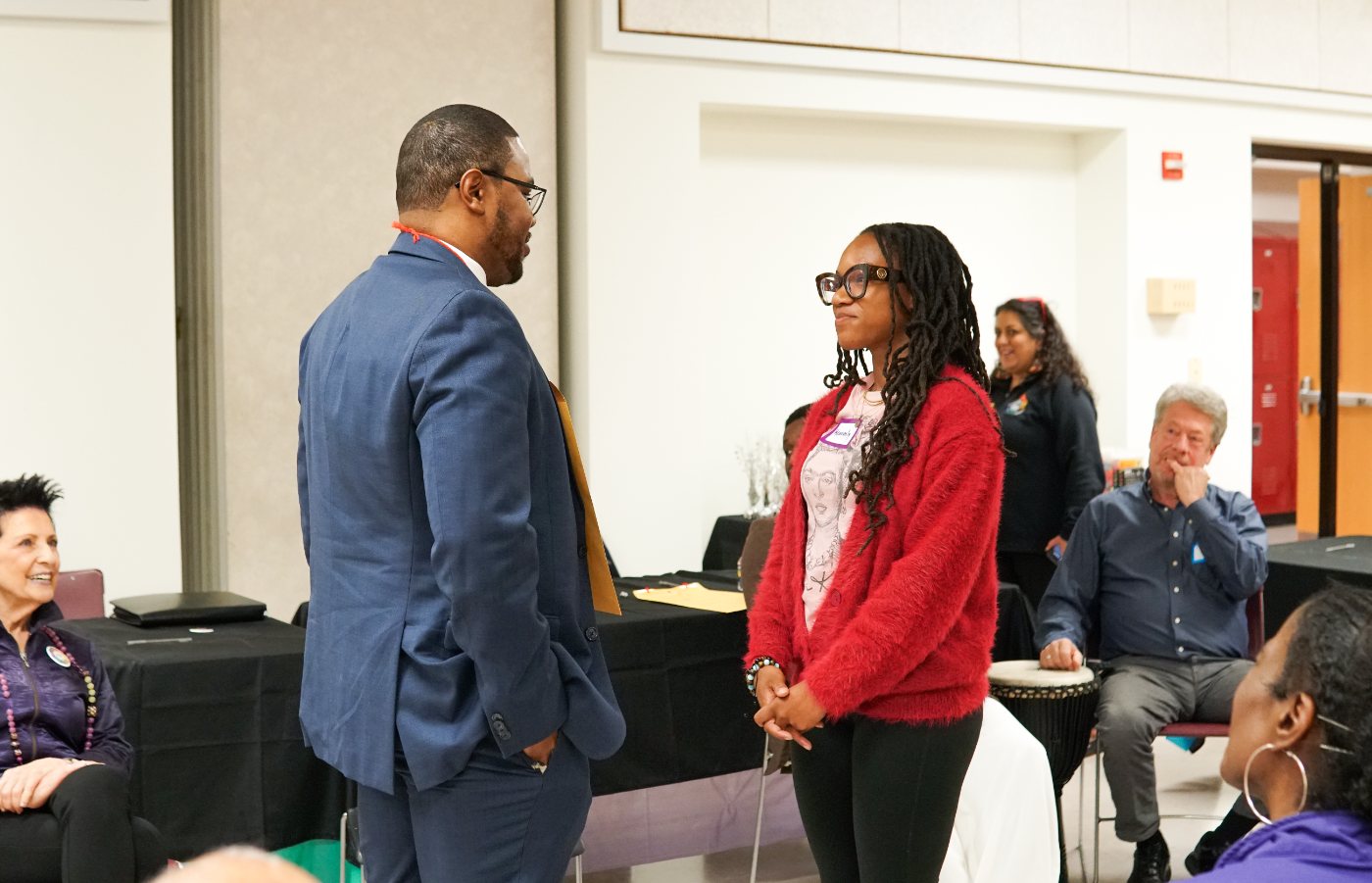 James Hollywood speaking with a young woman at a Life Pieces to Masterpieces event while attendees look on